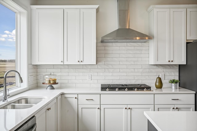 kitchen featuring tasteful backsplash, light countertops, appliances with stainless steel finishes, wall chimney exhaust hood, and a sink