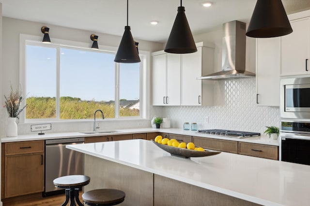 kitchen with light countertops, wall chimney range hood, appliances with stainless steel finishes, and a sink