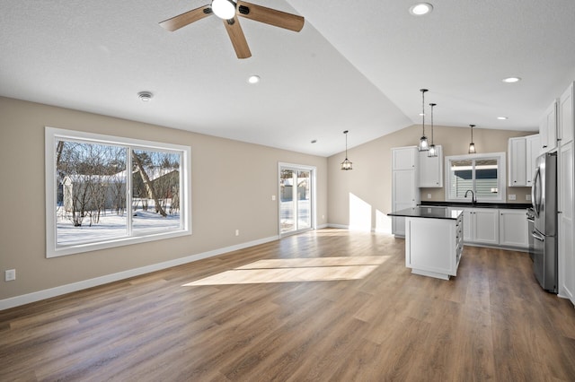 kitchen with dark countertops, open floor plan, vaulted ceiling, freestanding refrigerator, and plenty of natural light