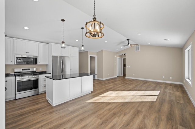 kitchen with lofted ceiling, white cabinets, appliances with stainless steel finishes, dark countertops, and ceiling fan with notable chandelier