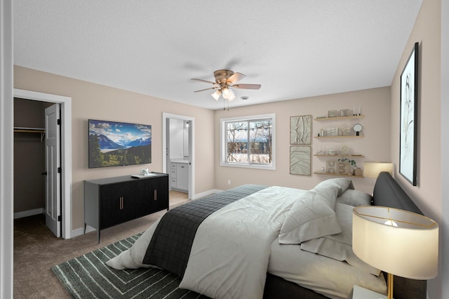 carpeted bedroom featuring a walk in closet, baseboards, ensuite bathroom, a closet, and a ceiling fan