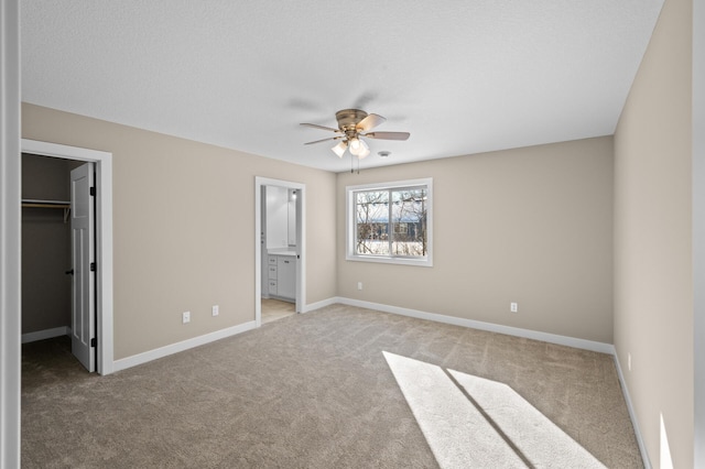 unfurnished bedroom featuring baseboards, a spacious closet, a closet, ensuite bathroom, and light carpet