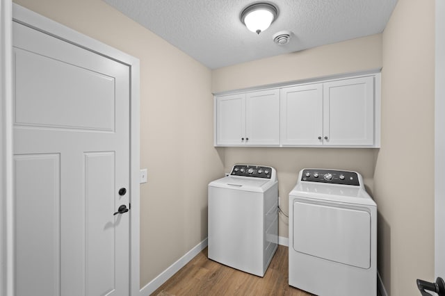 laundry room featuring a textured ceiling, wood finished floors, cabinet space, separate washer and dryer, and baseboards