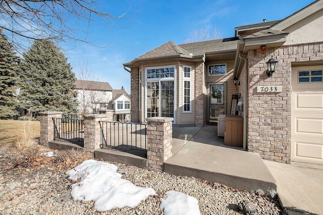 view of exterior entry featuring an attached garage and roof with shingles