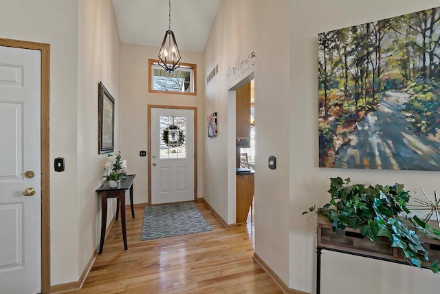 foyer entrance with visible vents, baseboards, light wood-style floors, and a notable chandelier