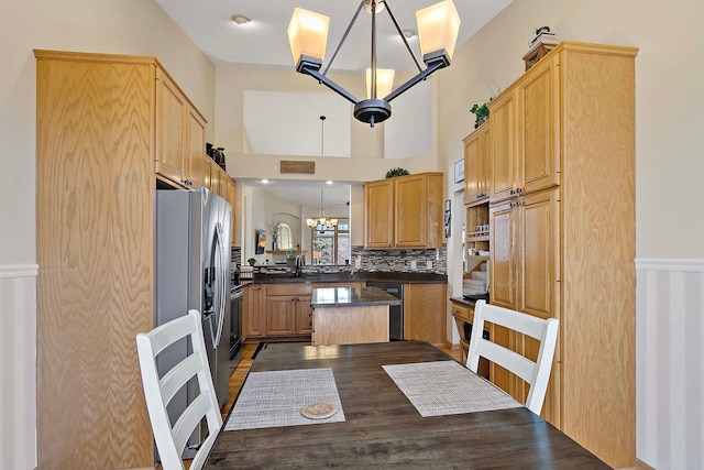 kitchen featuring dark countertops, a kitchen island, stainless steel fridge with ice dispenser, decorative backsplash, and a notable chandelier