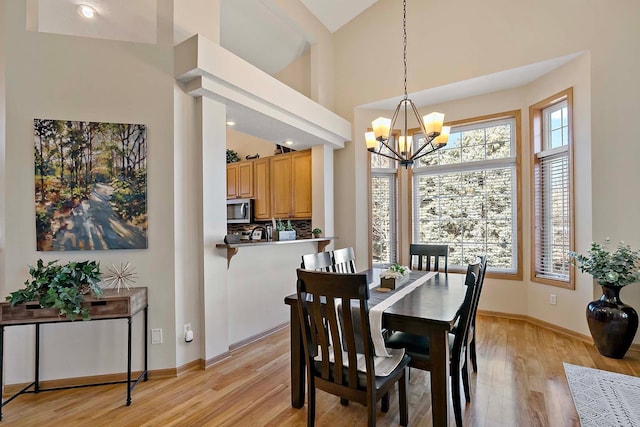 dining room with baseboards, light wood-style floors, a high ceiling, and a chandelier