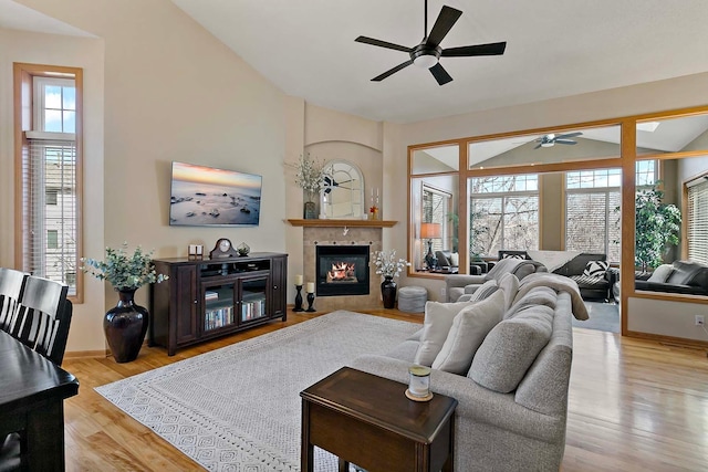 living area featuring a tiled fireplace, a ceiling fan, baseboards, and light wood finished floors