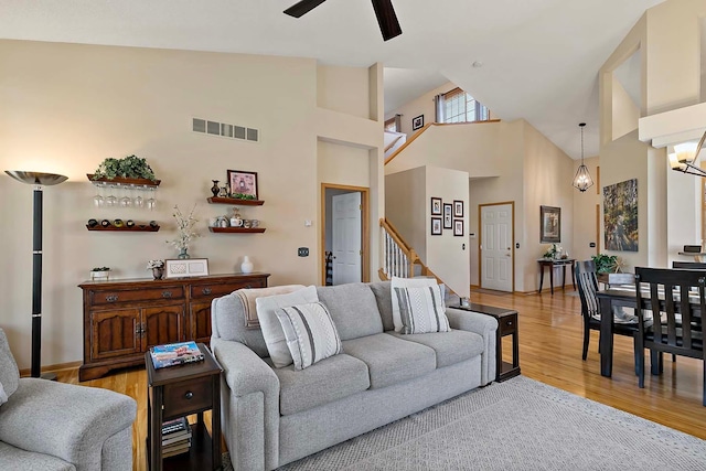 living room featuring visible vents, high vaulted ceiling, light wood-style flooring, a ceiling fan, and stairs