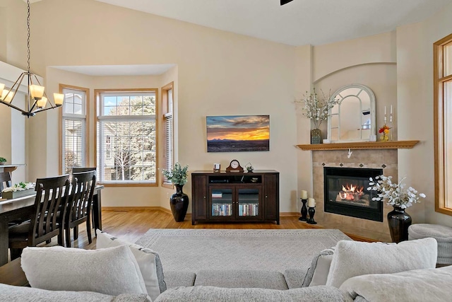 living area with a tiled fireplace, an inviting chandelier, wood finished floors, and baseboards