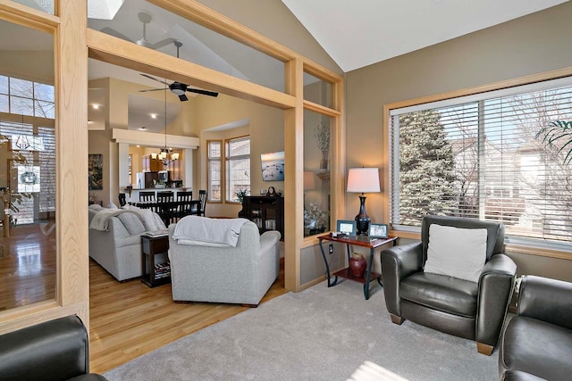 living area with ceiling fan with notable chandelier, wood finished floors, and vaulted ceiling