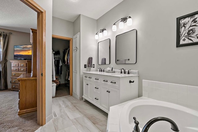 bathroom featuring a walk in closet, a garden tub, marble finish floor, a textured ceiling, and double vanity