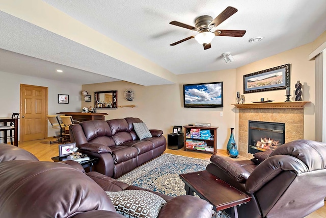 living room featuring a textured ceiling, light wood-style flooring, a fireplace, and ceiling fan