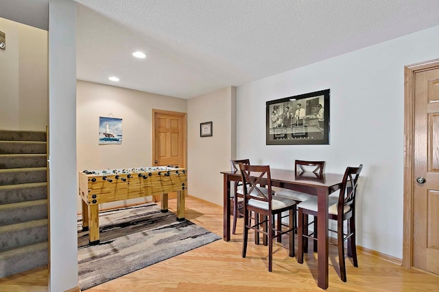 dining space with stairway, light wood-style floors, baseboards, and a textured ceiling