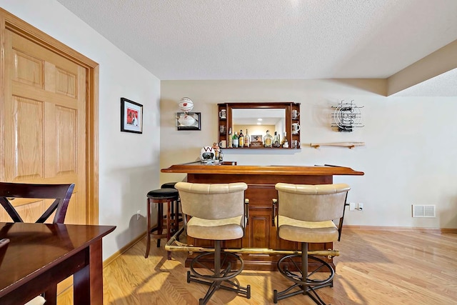 bar featuring light wood-type flooring, visible vents, a textured ceiling, baseboards, and a dry bar