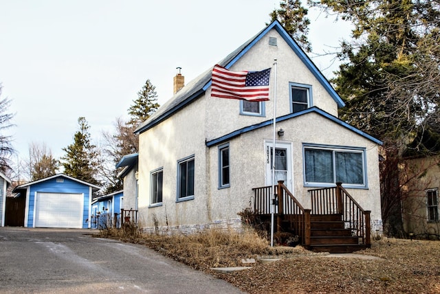 view of front of house with stucco siding, an outbuilding, driveway, a detached garage, and a chimney