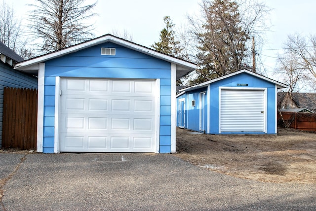 detached garage featuring driveway and fence