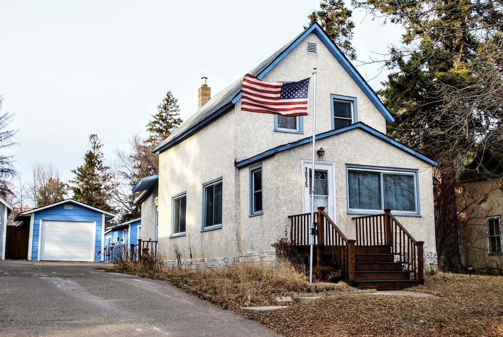 view of front of home featuring a detached garage, aphalt driveway, stucco siding, a chimney, and an outdoor structure