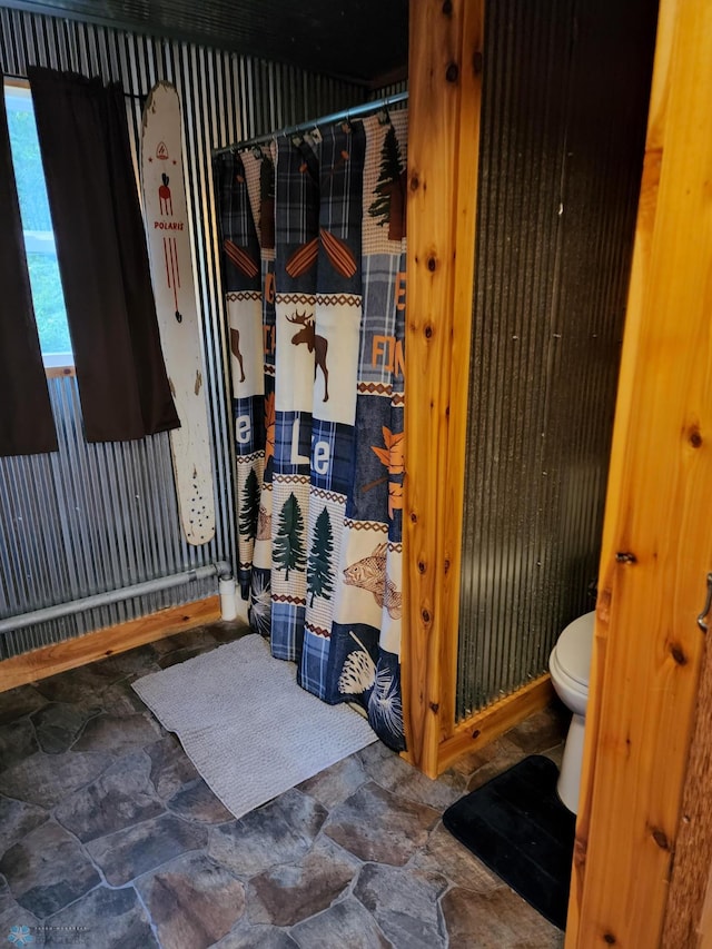 bathroom with toilet, stone finish floor, and a shower with curtain