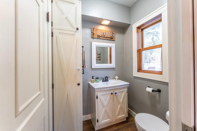 half bath featuring baseboards, toilet, wood finished floors, and vanity