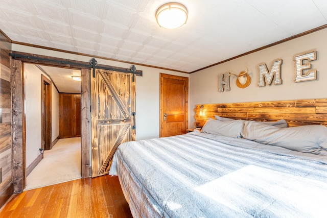 bedroom with a barn door, light wood-style floors, and crown molding