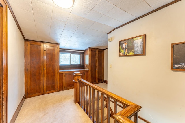 hallway with light carpet, an upstairs landing, crown molding, and baseboards