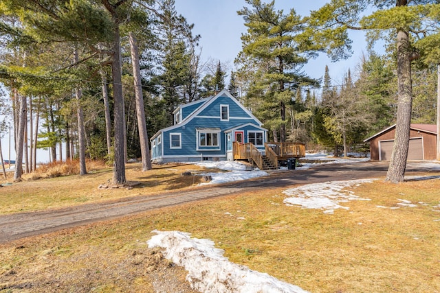 view of front of house featuring driveway, a detached garage, an outdoor structure, a front yard, and a wooden deck