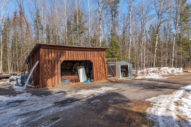 snow covered structure with an outdoor structure, a wooded view, and a pole building