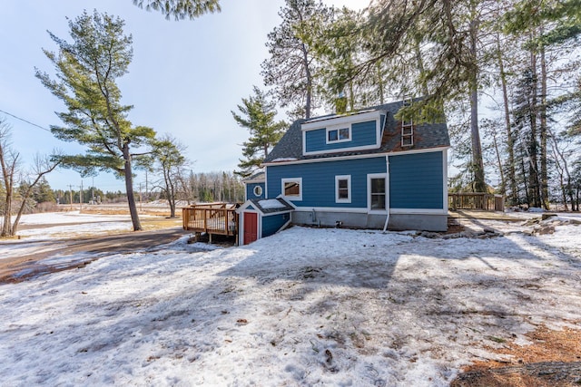 snow covered rear of property featuring a shingled roof and a wooden deck