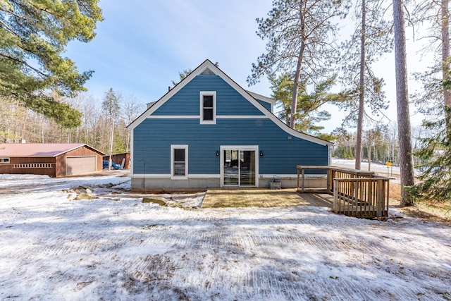 snow covered back of property with a garage and an outdoor structure