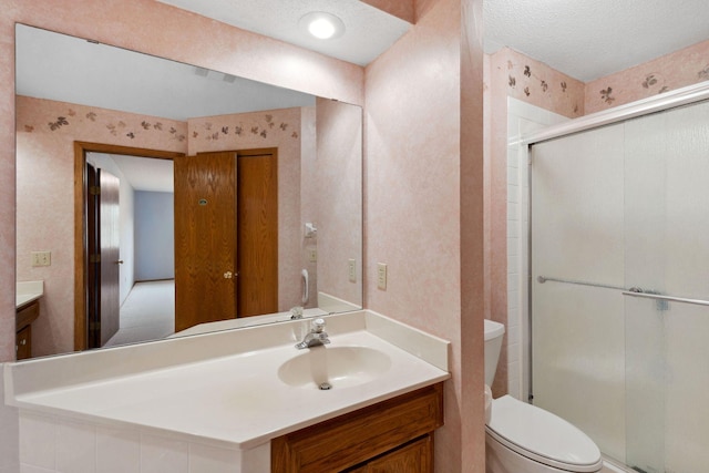 bathroom with vanity, wallpapered walls, a shower stall, a textured ceiling, and toilet