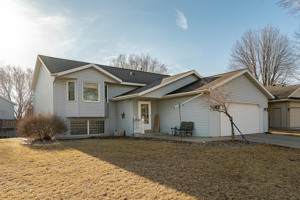 tri-level home with concrete driveway, a garage, a front yard, and a shingled roof
