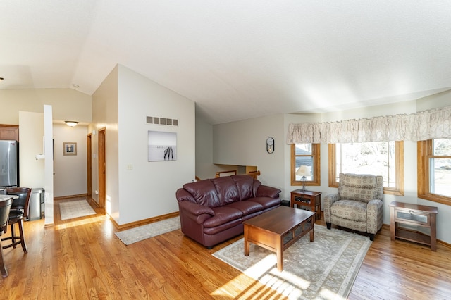 living room featuring visible vents, baseboards, light wood-style flooring, and vaulted ceiling