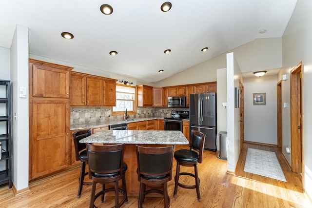 kitchen with a kitchen bar, brown cabinets, stainless steel appliances, decorative backsplash, and vaulted ceiling