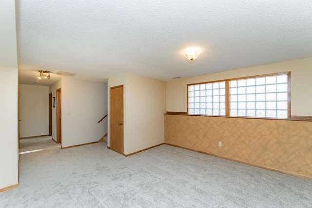 spare room featuring baseboards, light carpet, a textured ceiling, and wallpapered walls