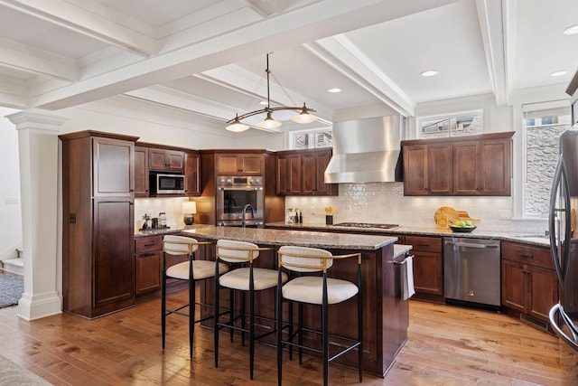 38 Mississippi River Blvd N, Saint Paul, MN 55104 - kitchen featuring appliances with stainless steel finishes, wall chimney range hood, light wood finished floors, beamed ceiling, and a kitchen bar