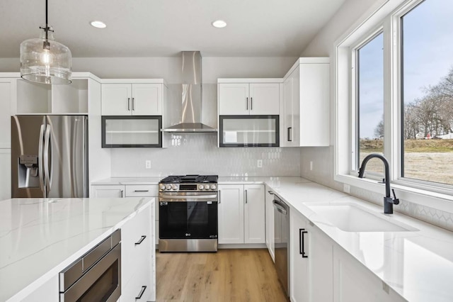 kitchen with a sink, stainless steel appliances, wall chimney exhaust hood, white cabinets, and light stone countertops