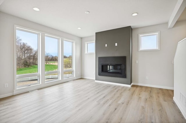 unfurnished living room with recessed lighting, light wood-style flooring, baseboards, and a glass covered fireplace