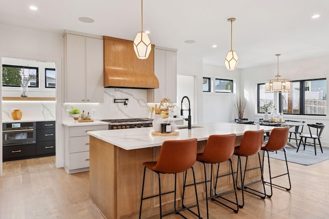 6008 Oaklawn Ave, Edina, MN 55424 - kitchen featuring black oven, recessed lighting, light wood finished floors, an island with sink, and light stone counters