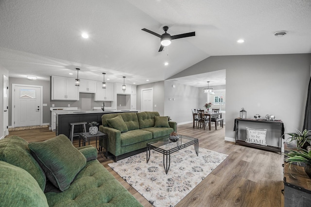 living area with baseboards, ceiling fan, lofted ceiling, light wood-style flooring, and a textured ceiling