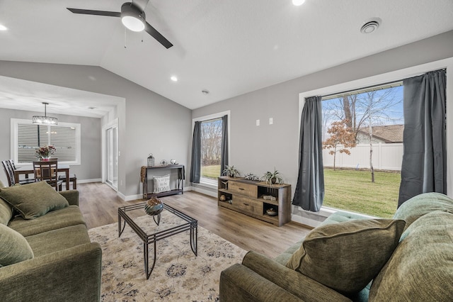 living area featuring vaulted ceiling, light wood-style flooring, ceiling fan with notable chandelier, and a wealth of natural light