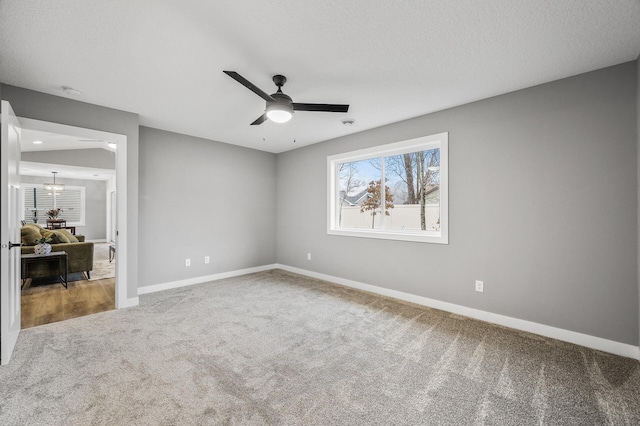 carpeted empty room featuring baseboards, a textured ceiling, and ceiling fan with notable chandelier