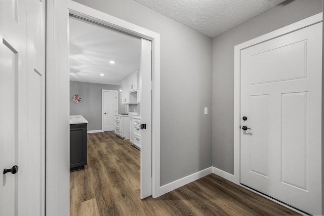 corridor featuring a textured ceiling, dark wood-type flooring, and baseboards