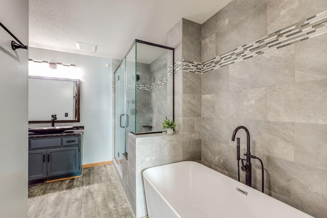 bathroom with vanity, wood finished floors, a freestanding tub, a shower stall, and a textured ceiling