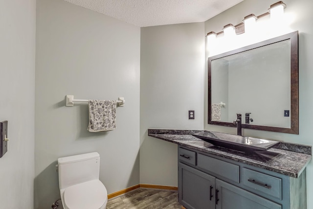 bathroom with baseboards, toilet, vanity, wood finished floors, and a textured ceiling