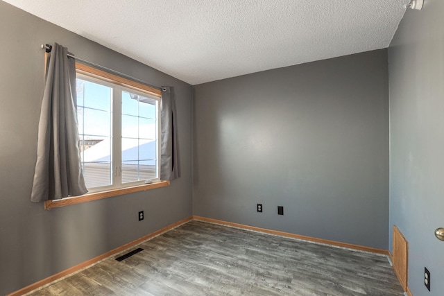 unfurnished room featuring visible vents, a textured ceiling, baseboards, and wood finished floors