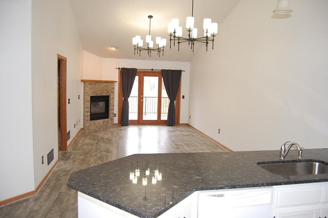 kitchen with wood finished floors, an inviting chandelier, white dishwasher, a sink, and white cabinets