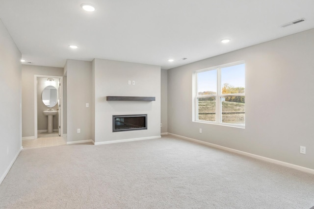 unfurnished living room with visible vents, baseboards, light colored carpet, recessed lighting, and a glass covered fireplace