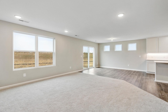 unfurnished living room with visible vents, baseboards, carpet, recessed lighting, and wood finished floors