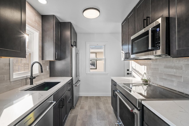 kitchen with a sink, light stone counters, baseboards, and appliances with stainless steel finishes